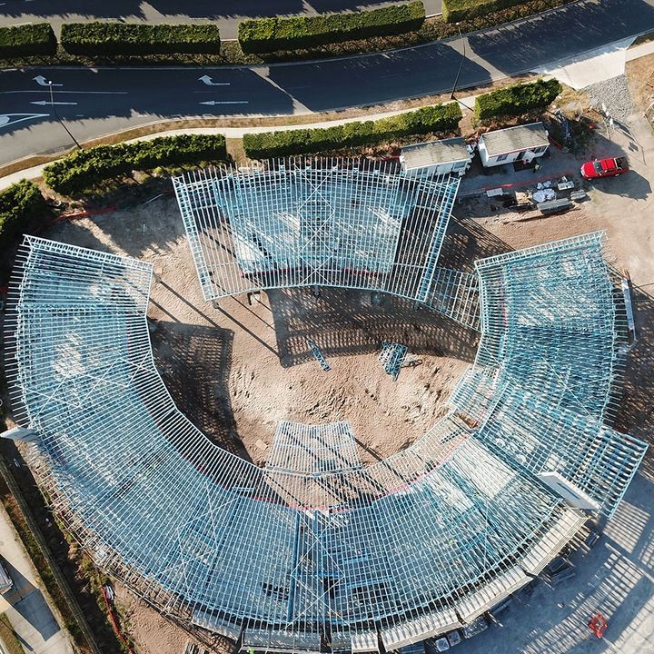 Aerial view of a curved childcare centre under construction, showcasing frames made from blue TRUECORE steel a dirt lot, surrounded by roads and greenery.