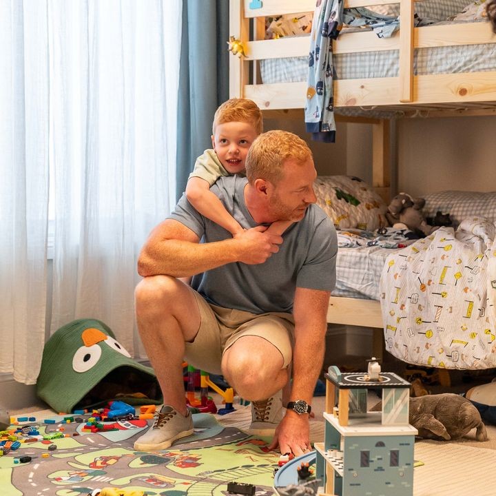Father and young son playing together in a colorful, toy-filled bedroom with bunk beds.