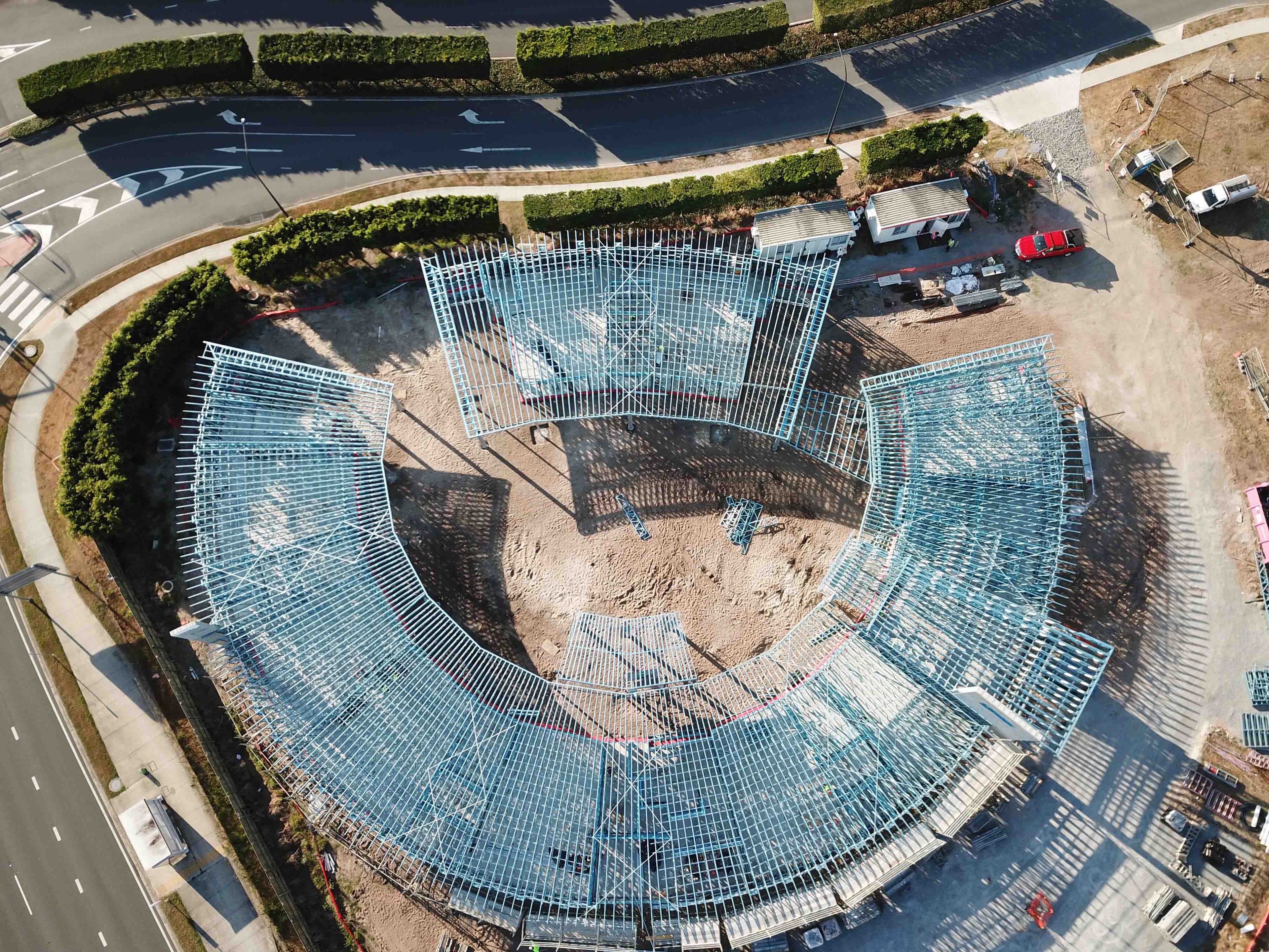 Top-down aerial view of a circular steel-framed building under construction, showing the structure's outline and surrounding area.